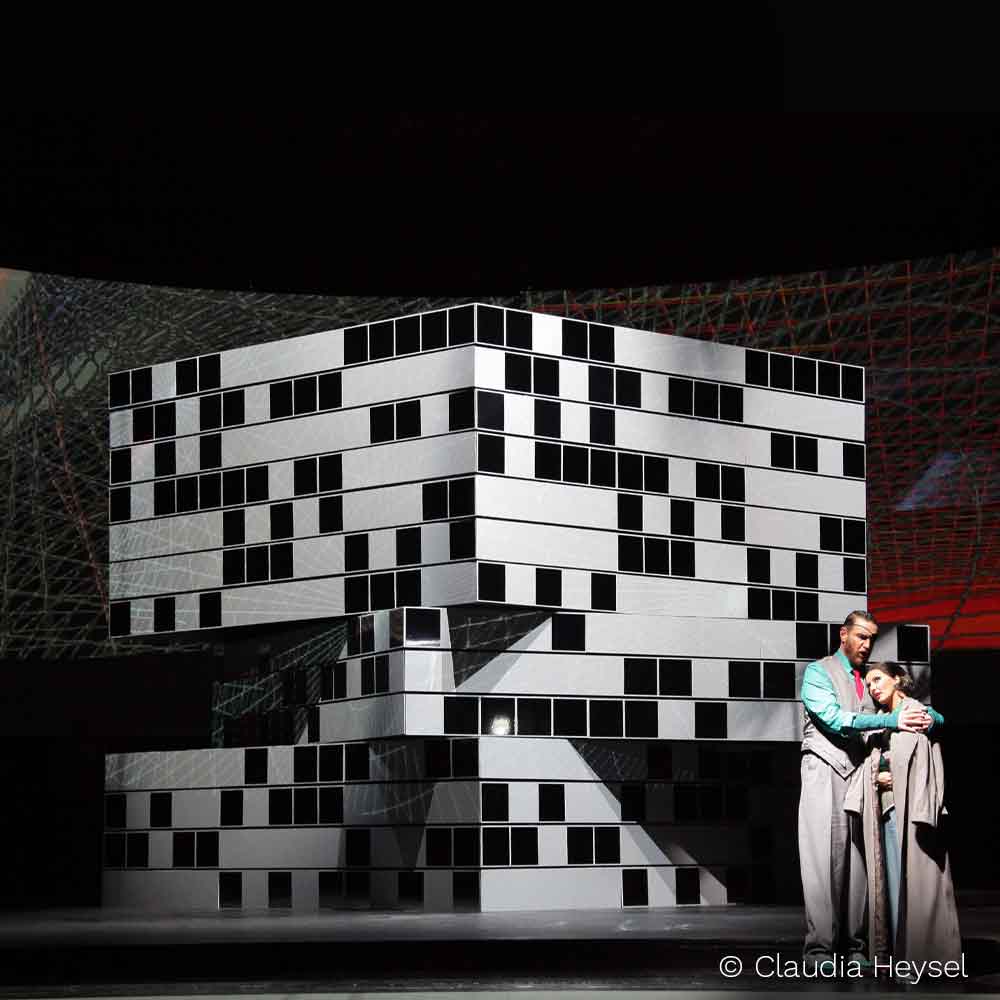 Schwarz-weißes Bühnenbild mit zwei Darstellern im Vordergrund