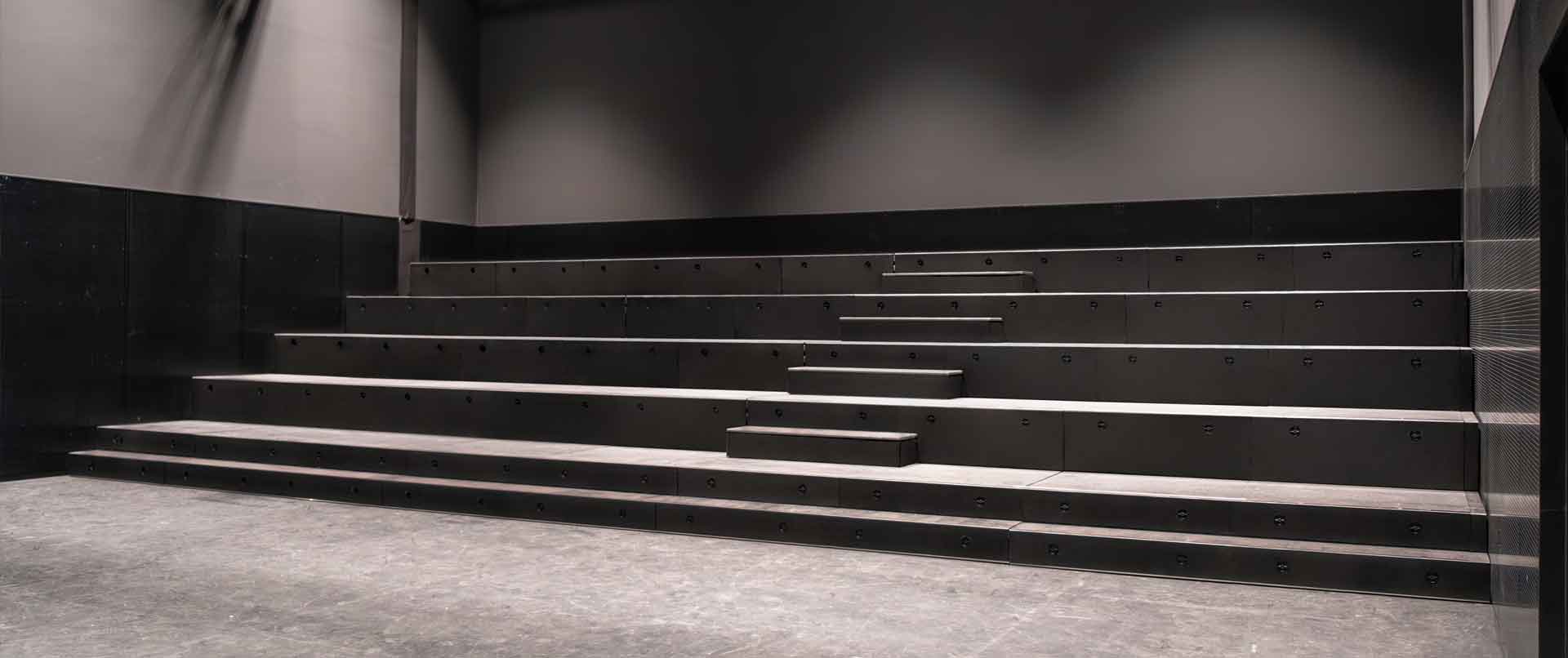 Leere schwarze Sitze in einem Auditorium mit stufenartiger Anordnung.