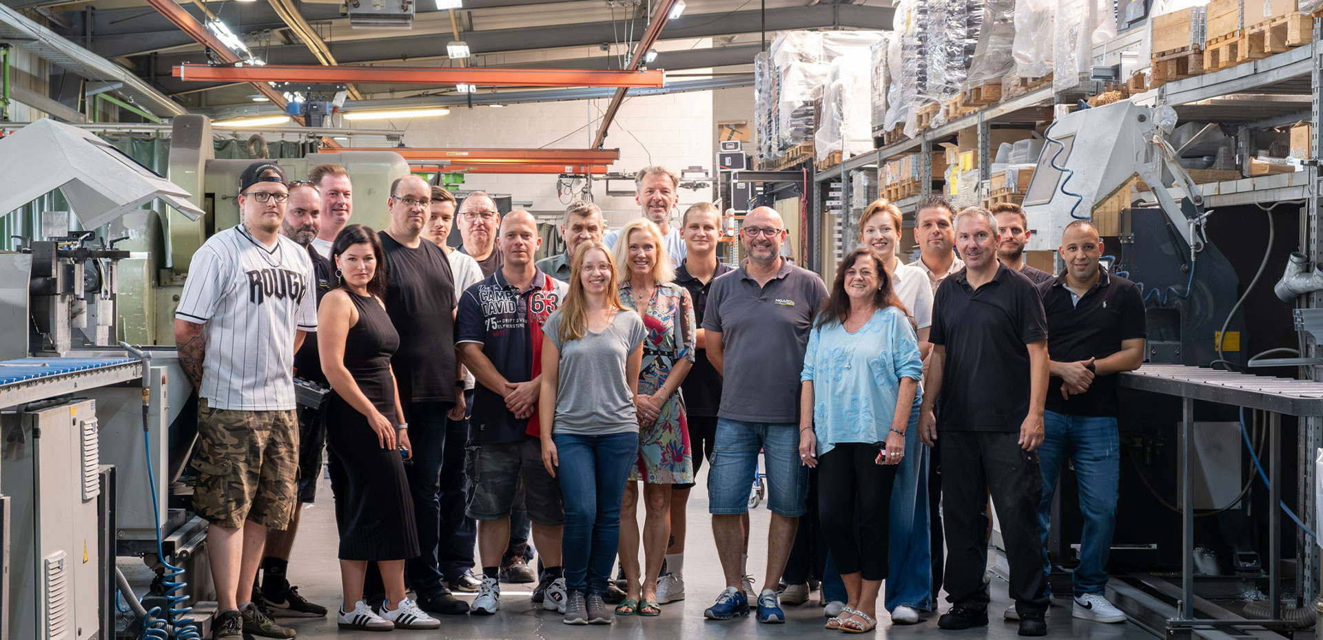 Eine Gruppe von etwa zwanzig Mitarbeitenden steht lächelnd in heller Fabrikhalle