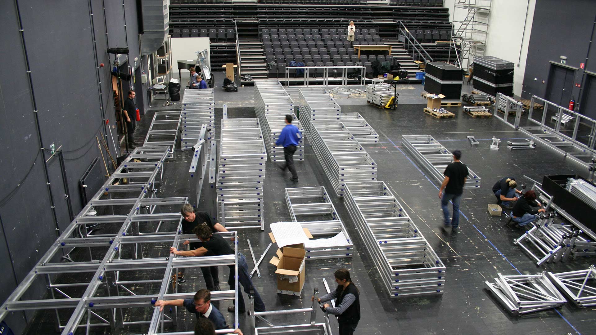 Mehrere Personen bauen mit silbernen Metallrahmen eine Bühnenkonstruktion auf