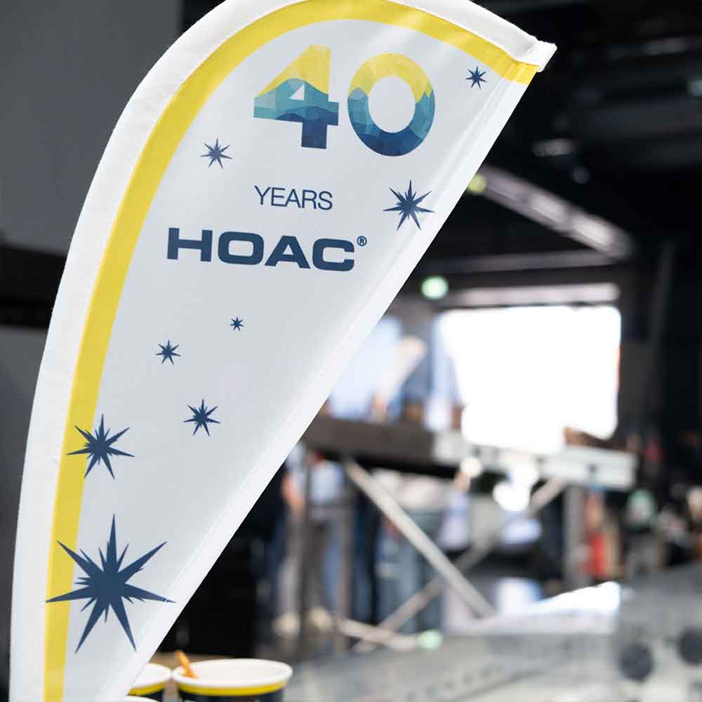 Eine weiße Flagge mit gelben und blauen Sternen feiert 40 Jahre HOAC in einer Halle