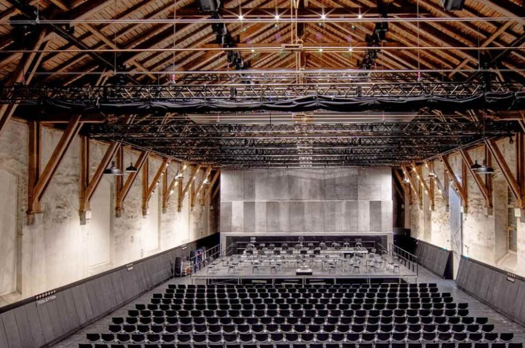 Leerer Konzertsaal in Grau und Braun mit Holzbalken und Stuhlreihen