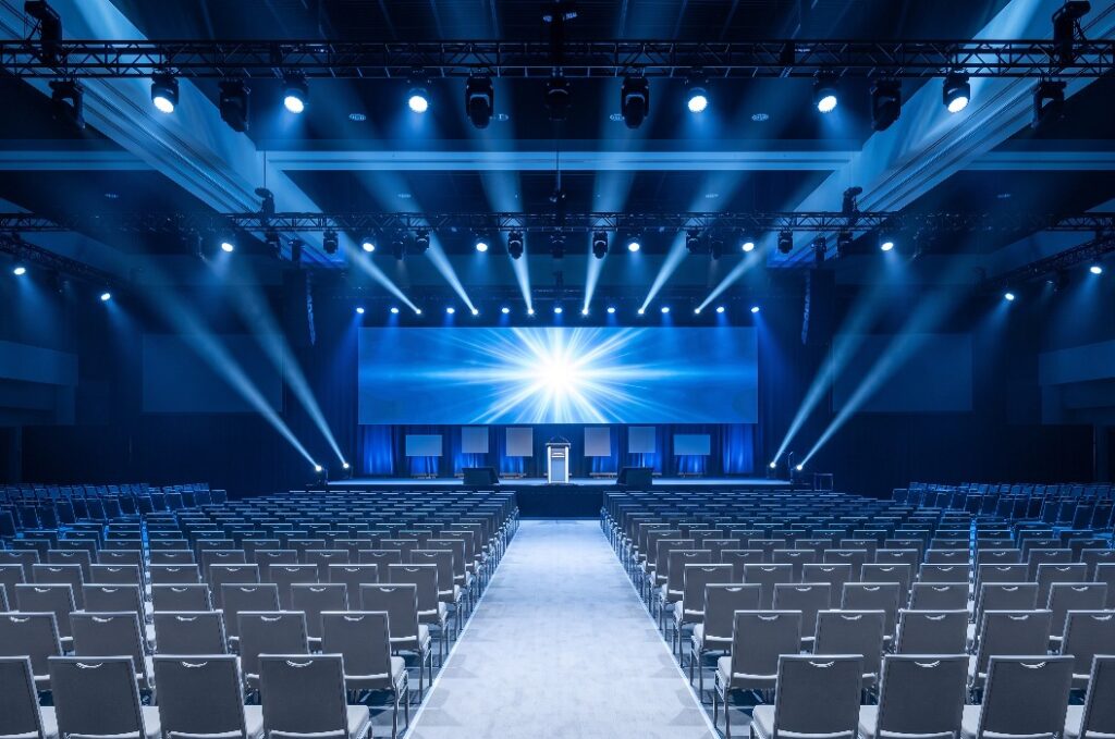 Leerer Konferenzsaal mit Bühne, heller Leinwand und Stuhlreihen in blauem Licht